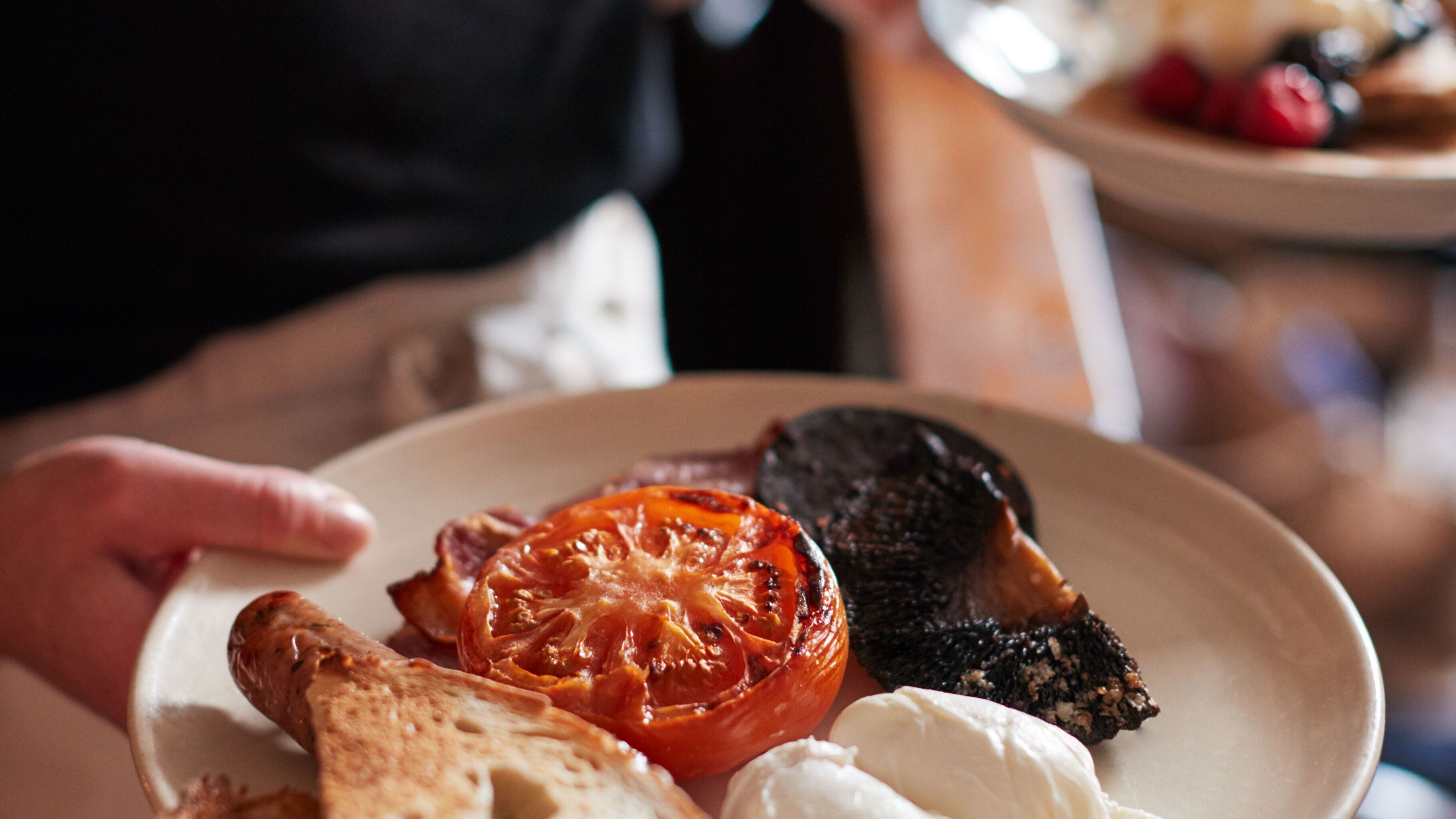 Une assiette avec une tomate rôtie, un morceau de viande et une tranche de pain.