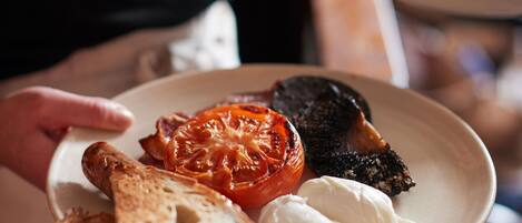 Une assiette avec une tomate rôtie, un morceau de viande et une tranche de pain.