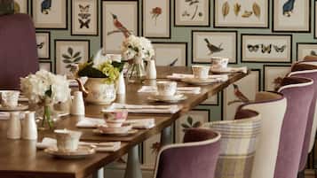 A dining table set with floral arrangements, teapots, and cups, surrounded by chairs with patterned cushions.