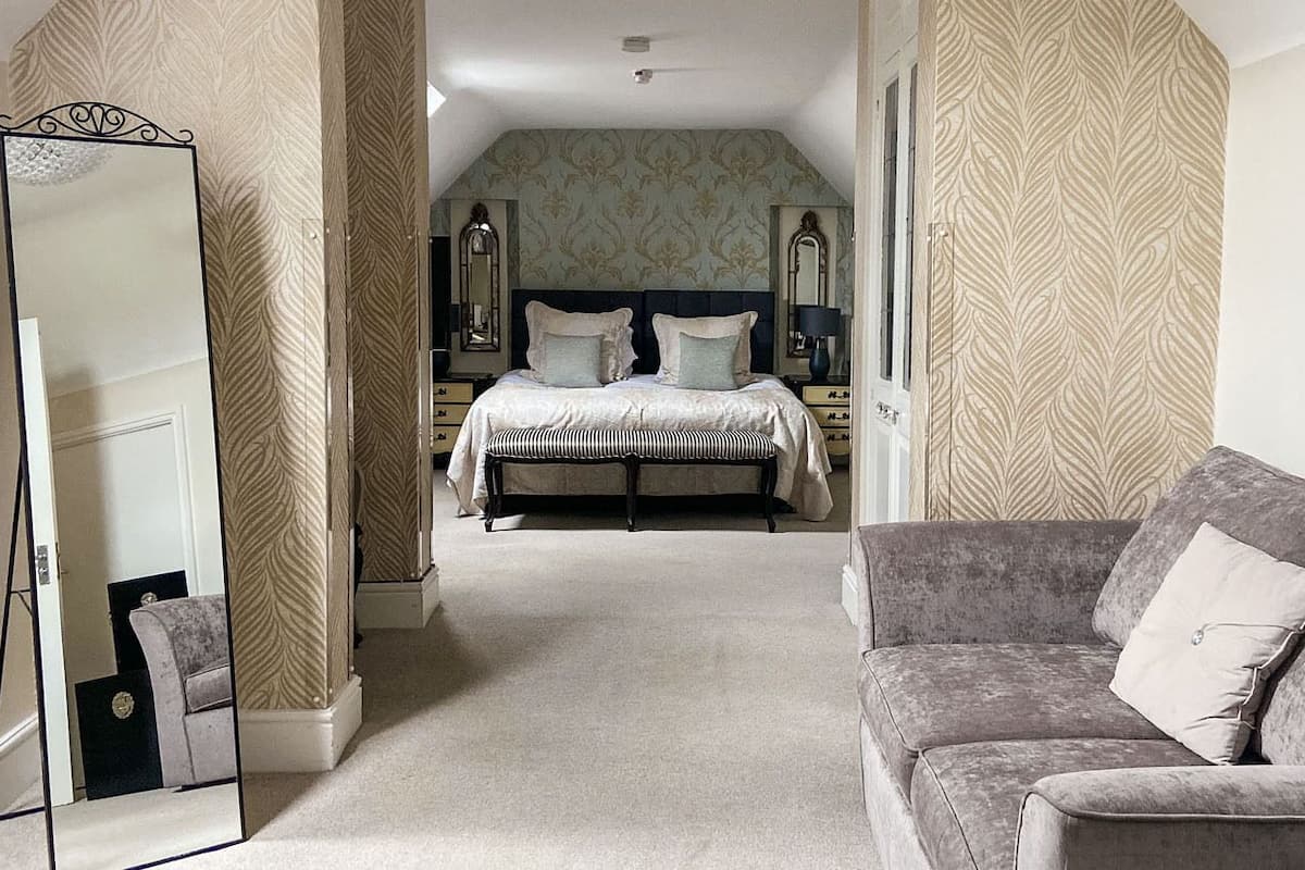 A bedroom with a bed, a mirror, a dresser, and a grey sofa.