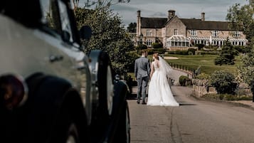 A wedding couple walking towards a stone building with a conservatory.