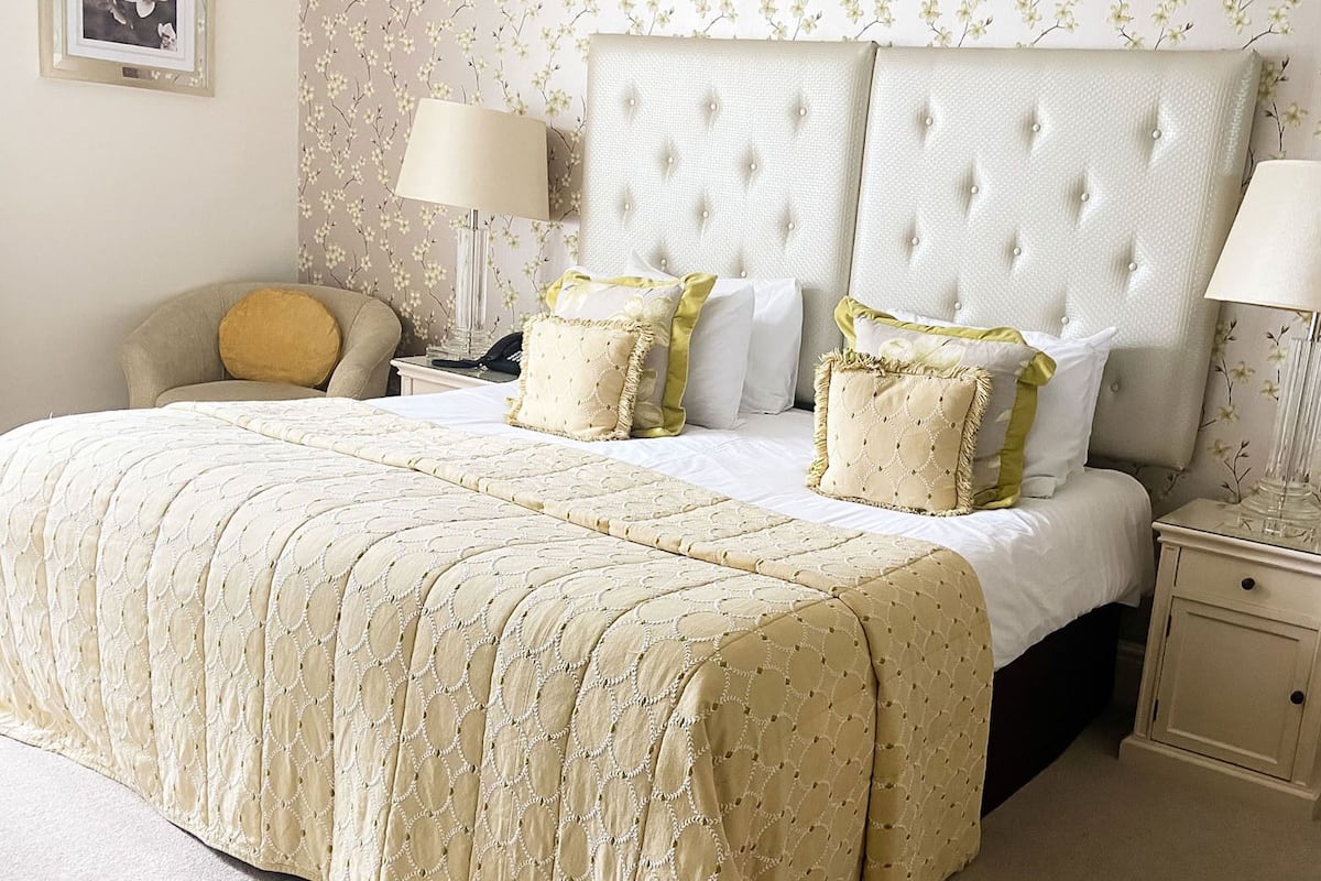 A neatly made bed with a quilted cover, two bedside lamps, and a nightstand with a vase.