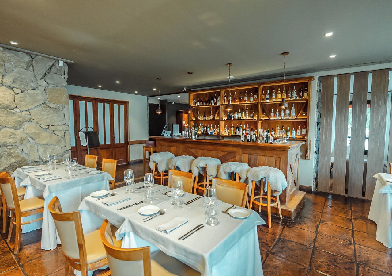 Un restaurant avec des tables dressées pour le service, un bar avec des étagères remplies de bouteilles et un mur en pierre.