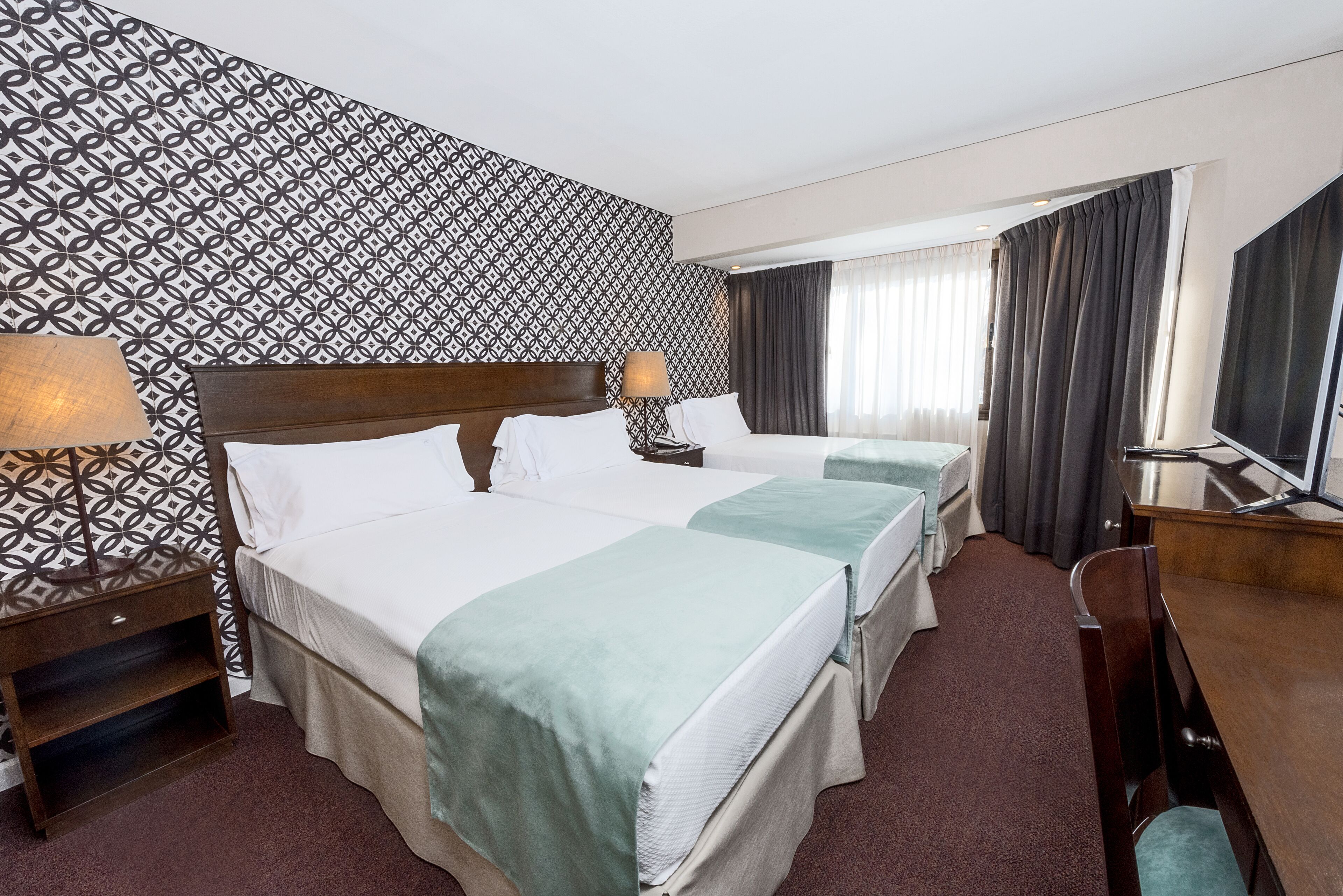 Una habitación de hotel con dos camas, un escritorio, un televisor y un papel tapiz estampado.