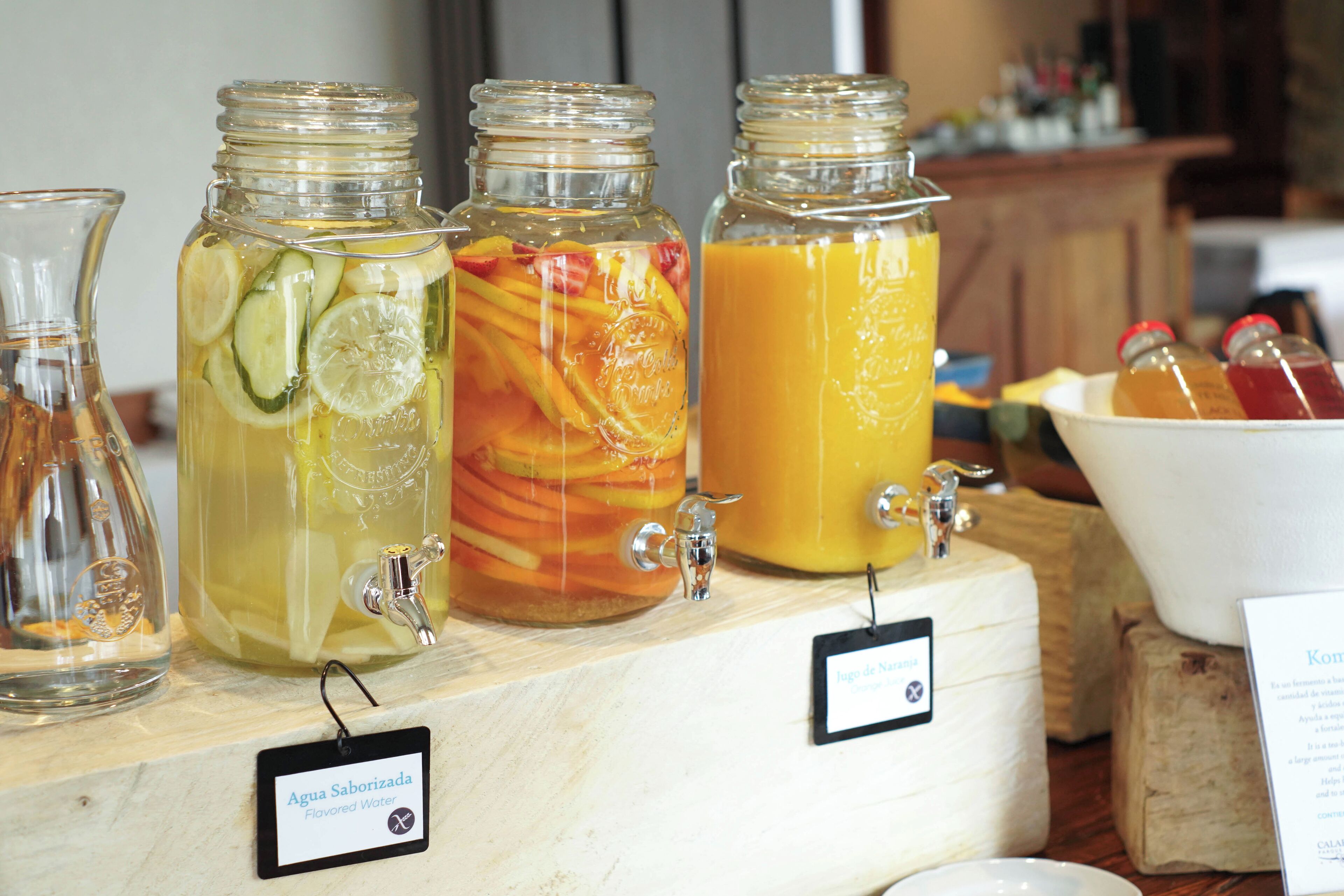 A beverage station with various drinks in glass jars, including a pitcher of water and a pitcher of orange juice.