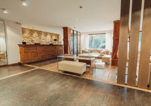A spacious living area with a stone wall, wooden furniture, and a large window offering a view of the outdoors. - Calafate Parque Hotel (El Calafate)
