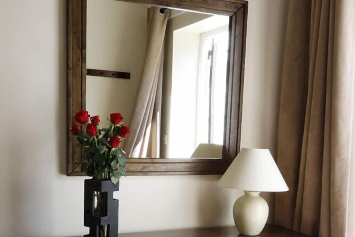 A wooden dresser with a mirror, a vase with red flowers, and a table lamp.