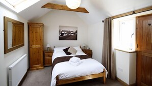 A bedroom with a sloped ceiling, wooden wardrobe, a bed with white linens, a bedside table with a lamp, and a picture on the wall. - Barker Stakes Farm B&B (Pickering)
