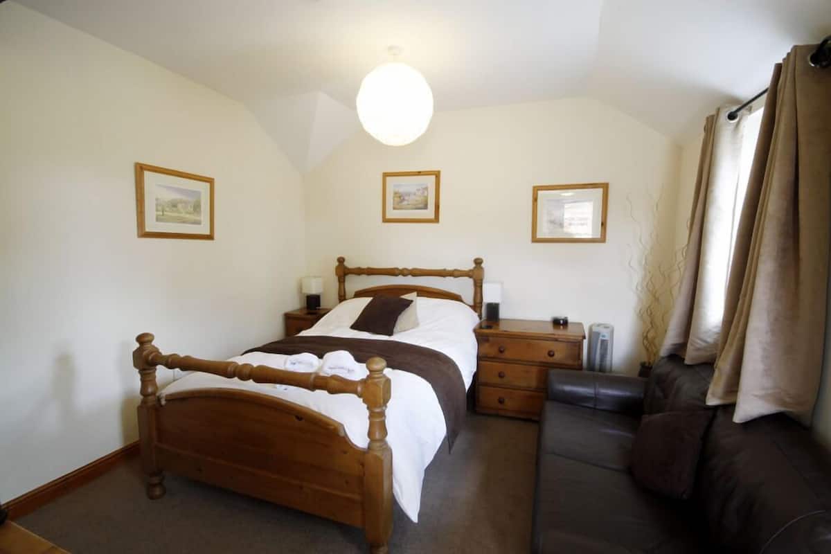 A bedroom with a wooden bed, bedside tables, a dresser, and a brown leather sofa.