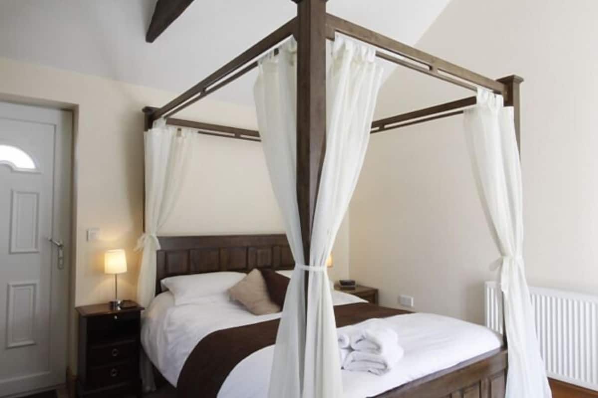 A four-poster bed with white drapes, a wooden headboard, and a bedside table with a lamp.