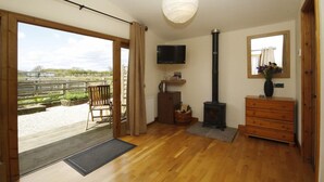 A spacious room with a large sliding glass door leading to an outdoor area, a wooden bench, a television mounted on the wall, a fireplace, and a dresser with a mirror. - Barker Stakes Farm B&B (Pickering)