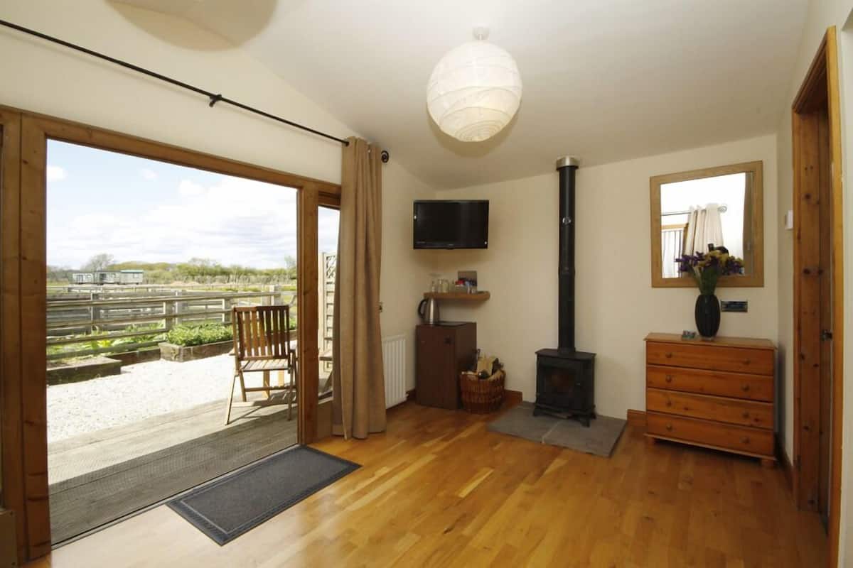 A spacious room with a large sliding glass door leading to an outdoor area, a wooden bench, a television mounted on the wall, a fireplace, and a dresser with a mirror.