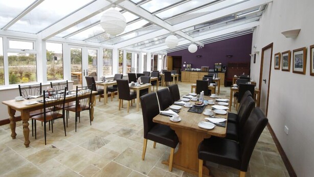 A spacious indoor area with multiple dining tables and chairs, a kitchen area, and large windows allowing natural light. - Barker Stakes Farm B&B (Pickering)