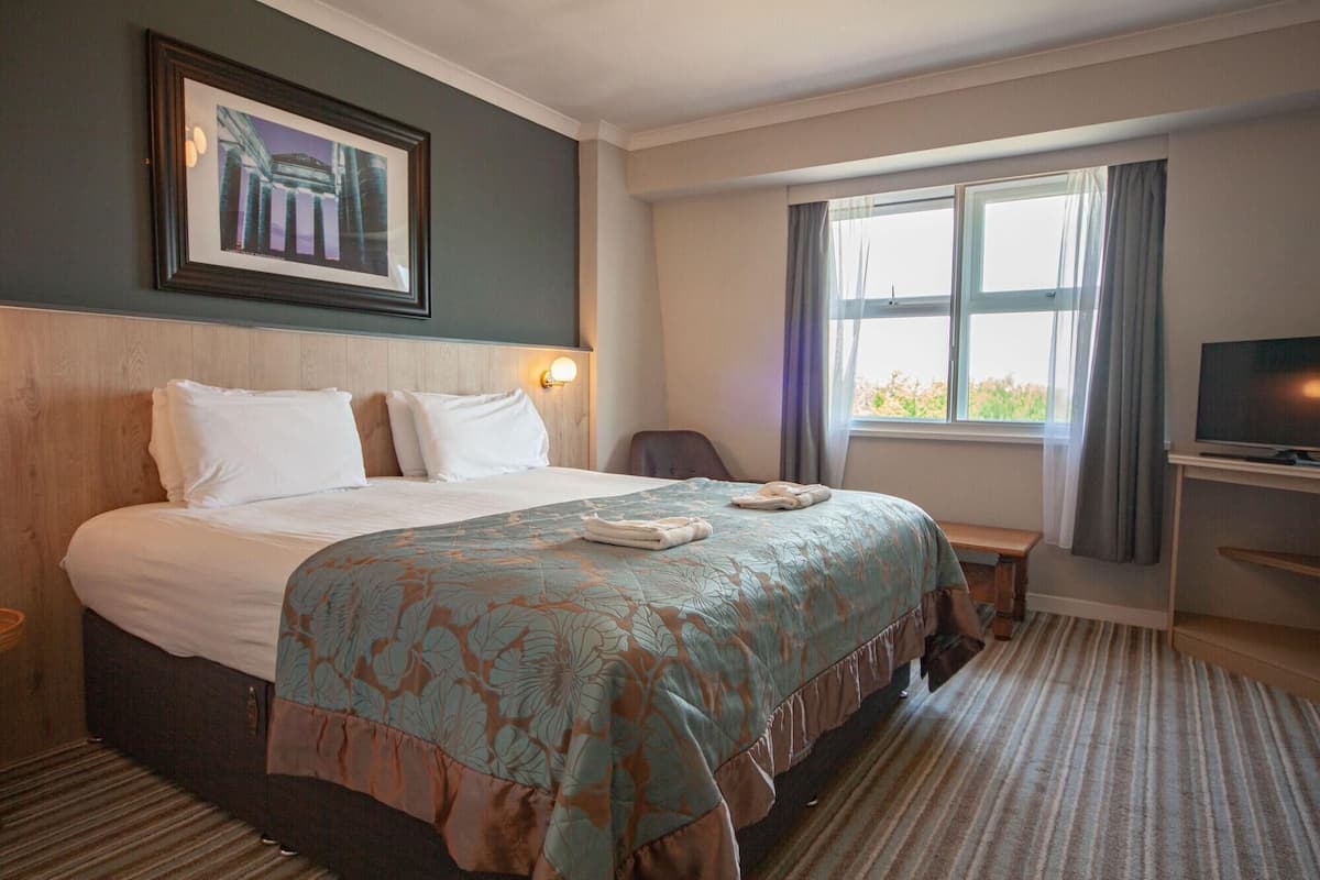 A hotel room with a bed, a television, a desk, and a window with curtains.