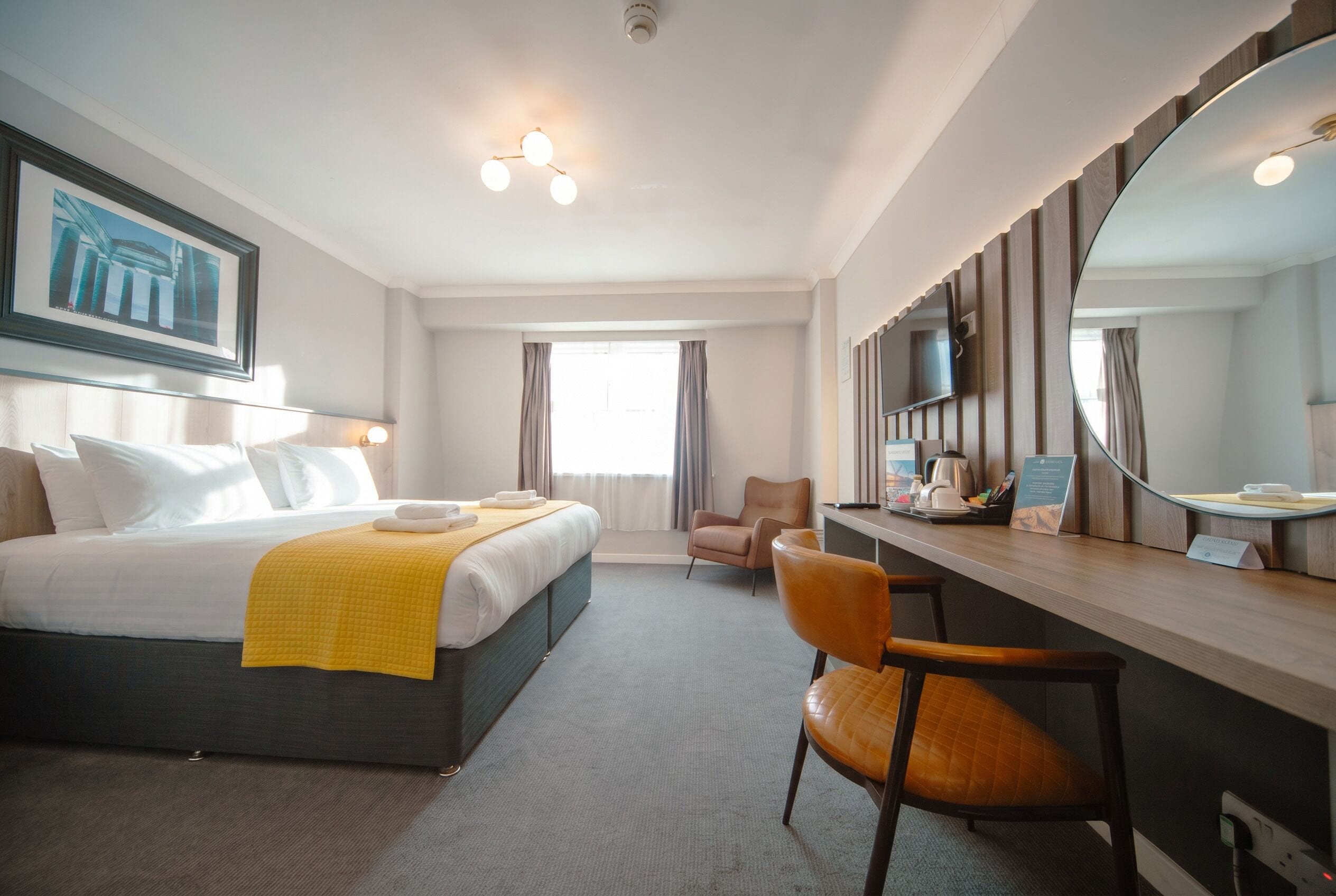 Ein Hotelzimmer mit einem Bett, einem Schreibtisch, einem Stuhl, einem großen Spiegel und einem Fernseher.
