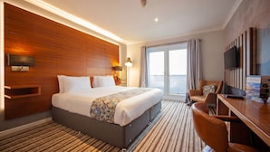 Habitación de hotel con una cama grande, un escritorio con una silla, un televisor y vista al mar.