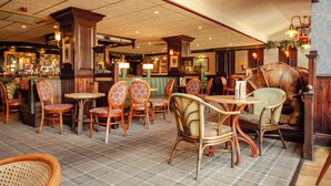 Interior de un restaurante con mobiliario de madera, una zona de bar y una estatua decorativa de un caballo.