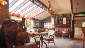 Interior de restaurante con mobiliario de madera, una gran escultura de madera y un techo alto con tragaluces.