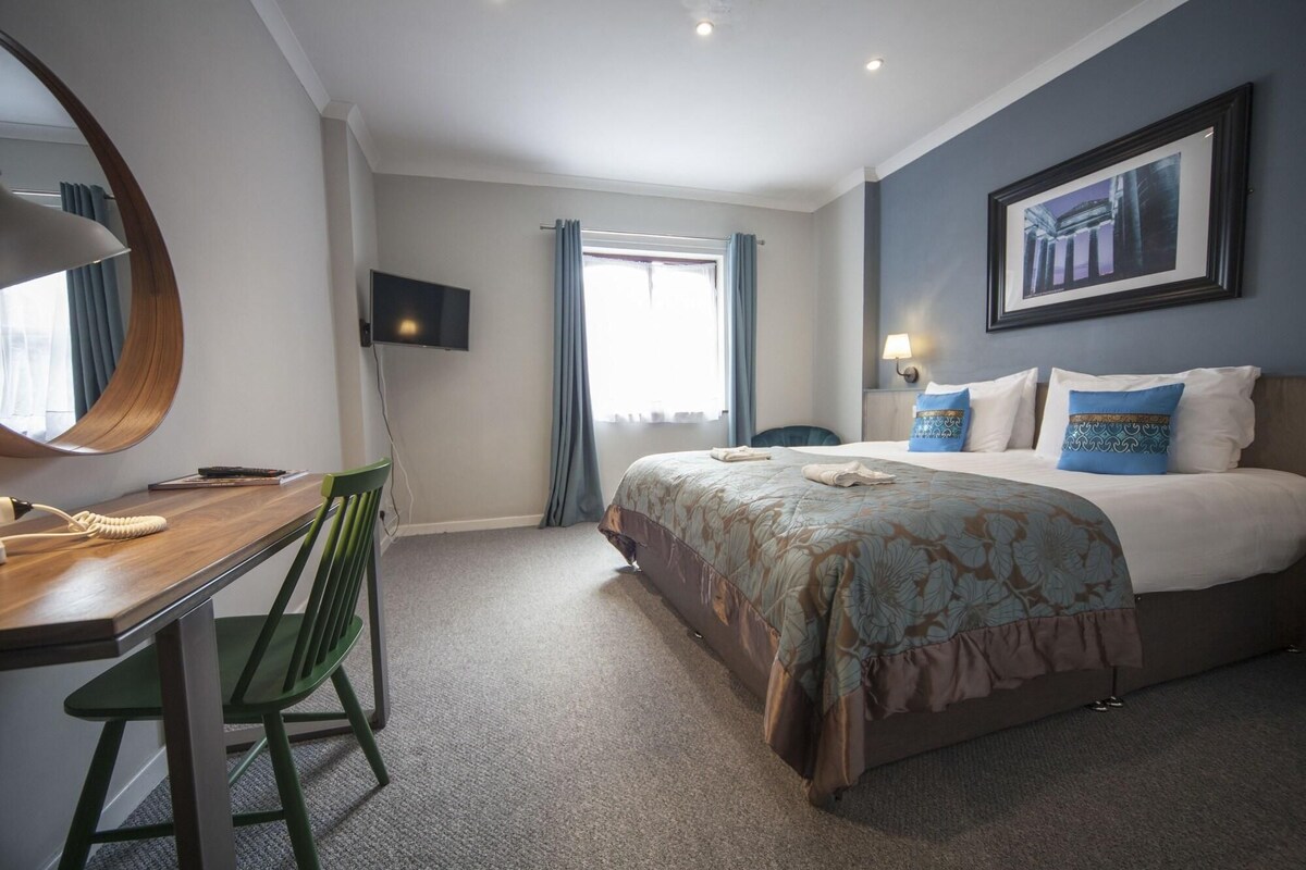 A hotel room with a bed, a desk, a chair, a TV, and a window with curtains.