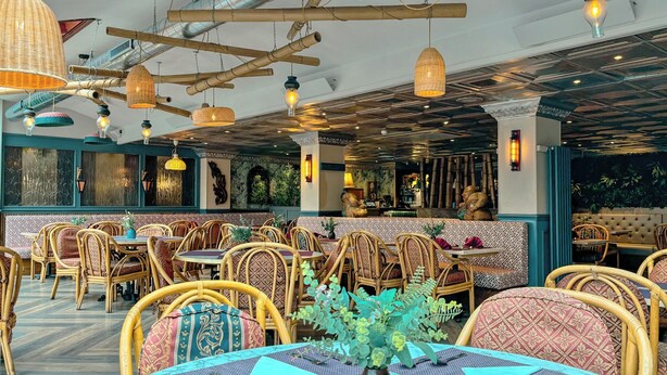 Un restaurante con mobiliario de mimbre, luces colgantes y un techo con motivos.