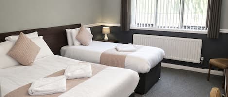 A hotel room with two beds, a radiator, a window with curtains, and a small table.