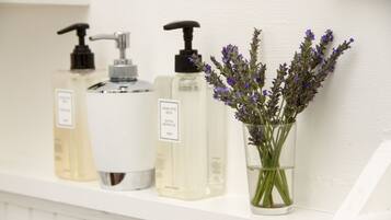A shelf with three bottles of liquid soap and a glass vase with lavender flowers.