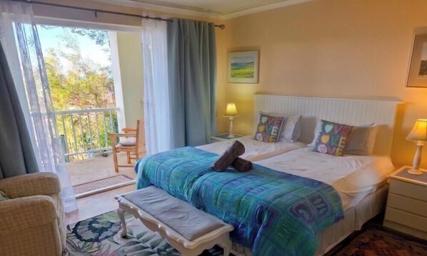 A bedroom with a bed, bench, nightstands, and a view of the outdoors. - Albatross Guest House (Cape Town)