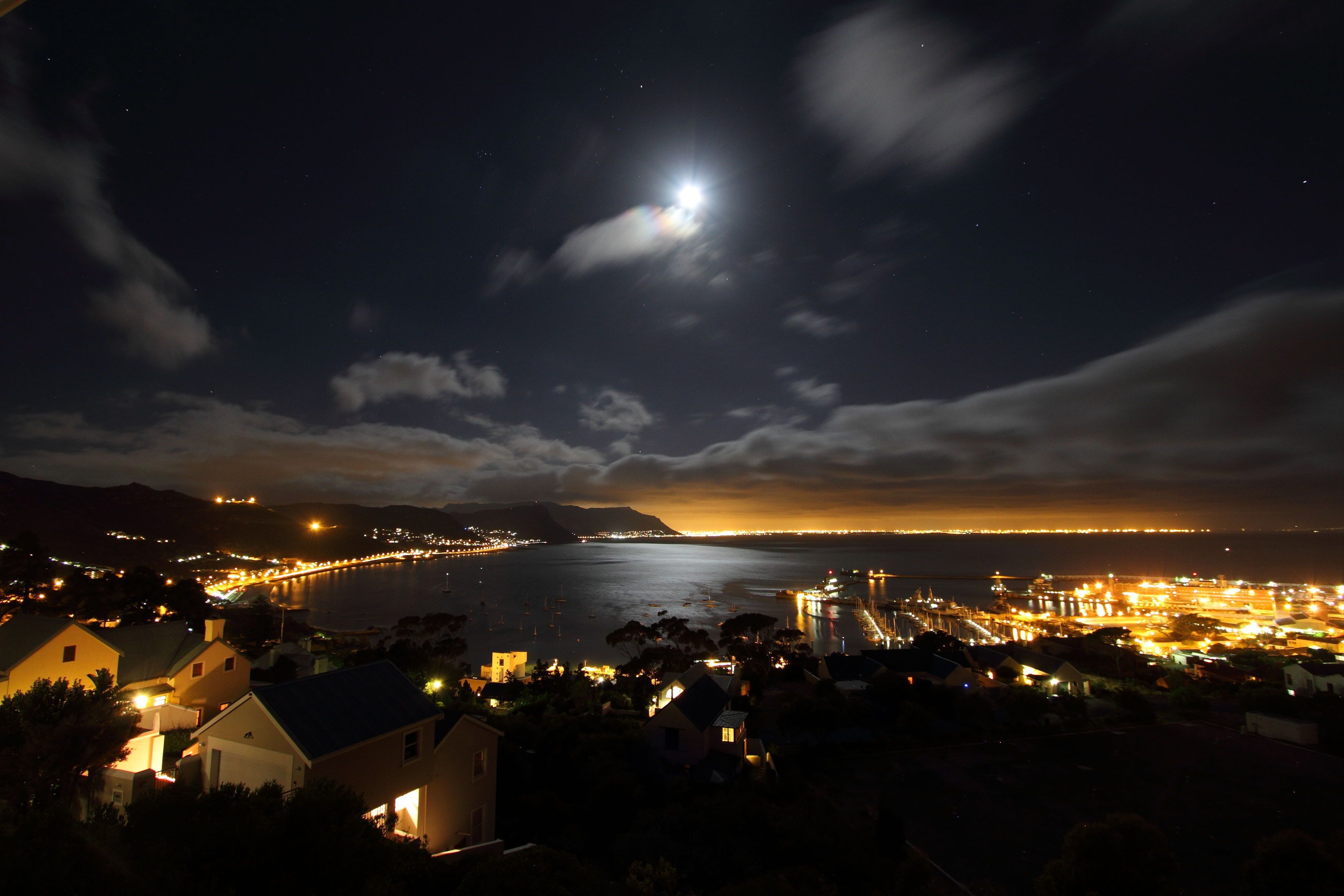 A coastal town at night with a prominent moon, a lit harbor, and residential buildings.