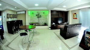 Una sala de estar con sofá, una mesa de comedor con sillas, un televisor y una pared con un panel decorativo verde.