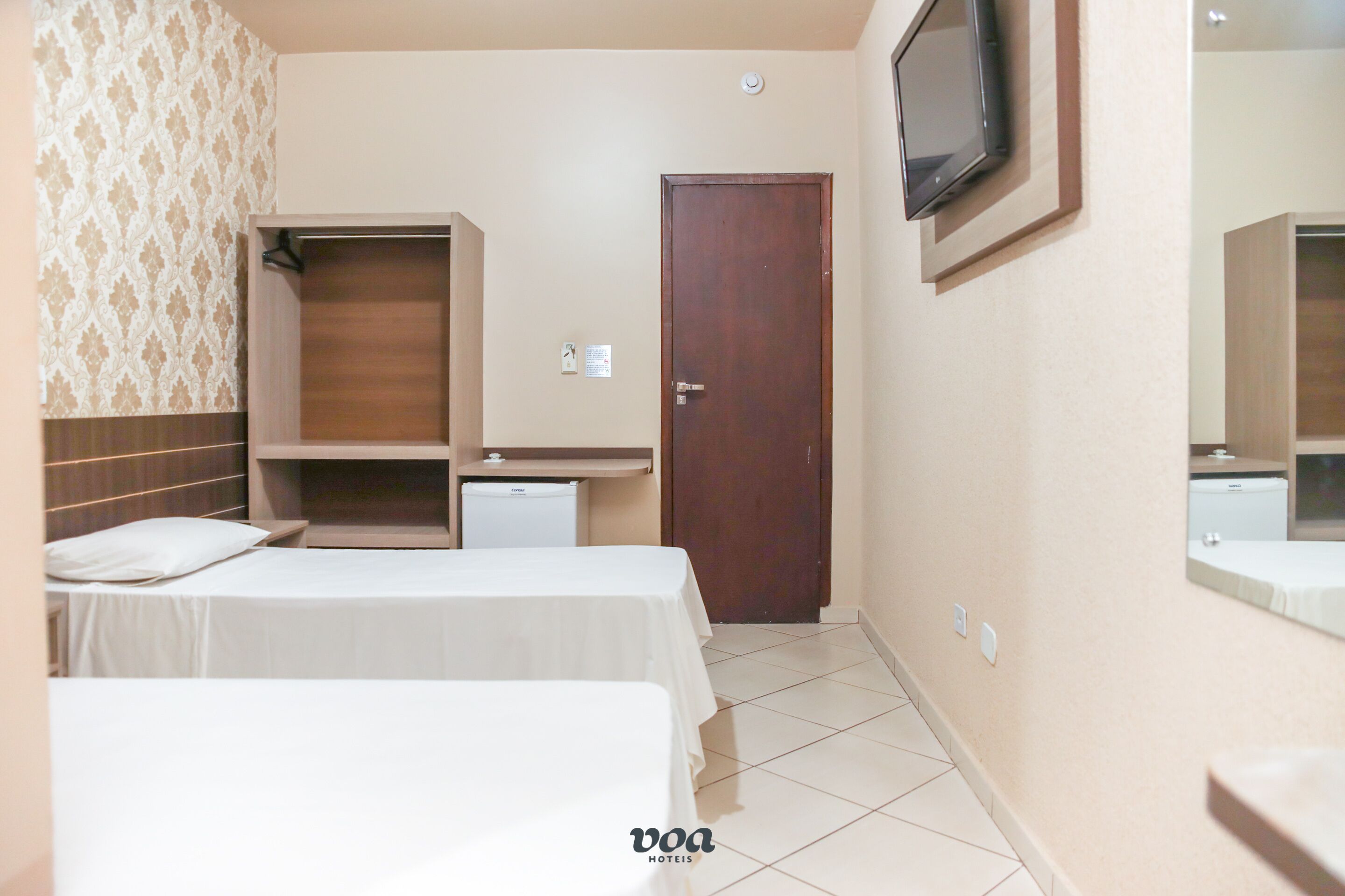 Habitación de hotel con dos camas, un armario, un escritorio, un televisor y un espejo de baño.