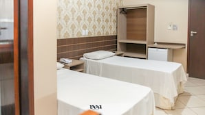 Habitación de hotel con dos camas, una mesita de noche con teléfono, un armario y un refrigerador pequeño.
