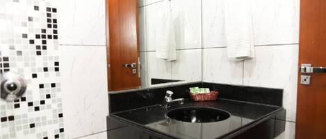Un baño con un lavabo negro, paredes cubiertas de azulejos blancos y puertas de madera.