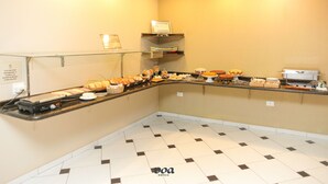 Zona de bufé con diversas opciones de comida, un expositor de vidrio y piso de baldosas.