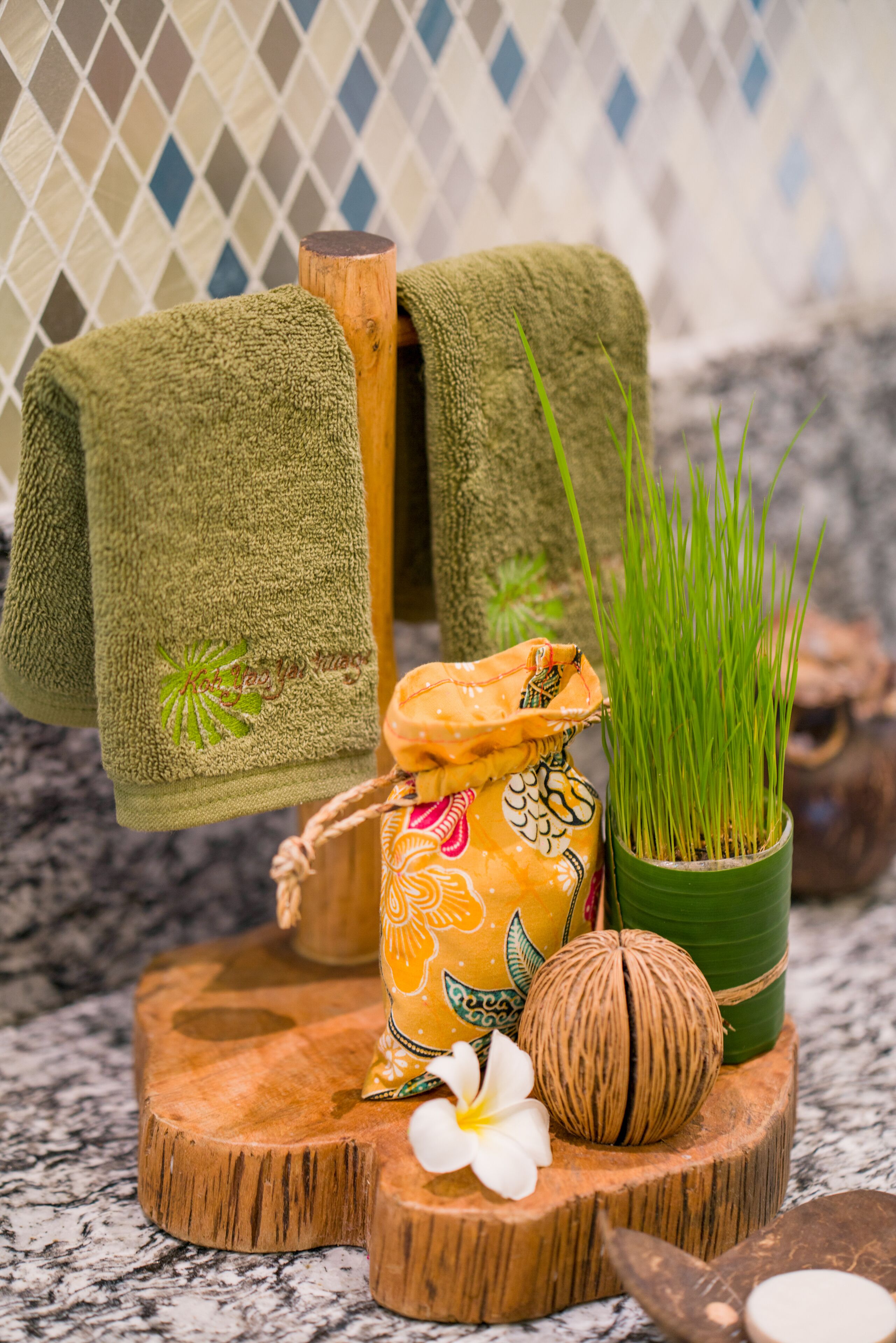 Un plateau en bois avec une serviette, un récipient décoratif, une plante en pot, une fleur et une noix de coco.