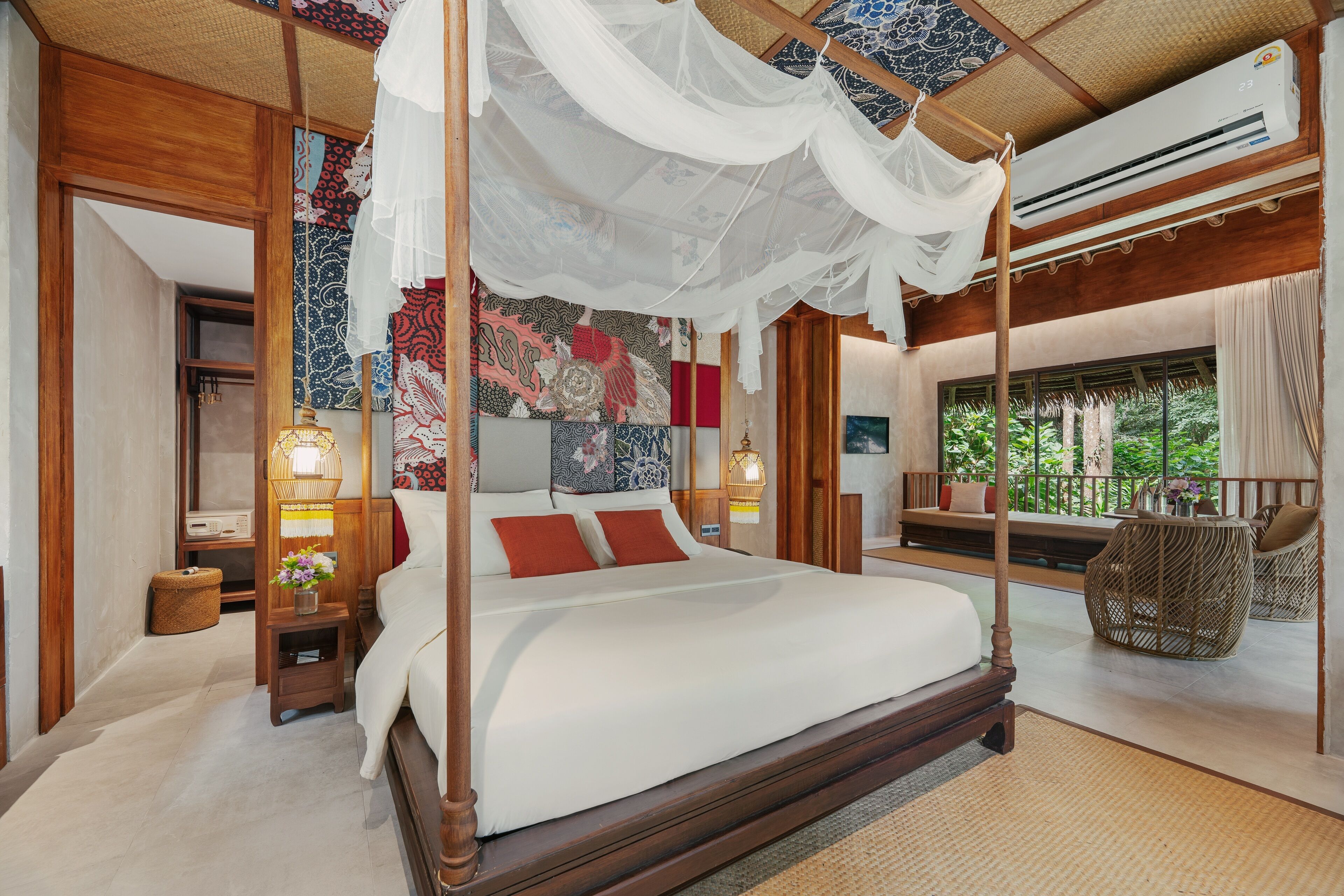 Una cama con dosel y cuatro columnas, una mesita de noche con lámpara, y vista al exterior a través de una ventana.