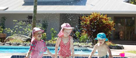 Three children playing in a swimming pool with a house in the background.