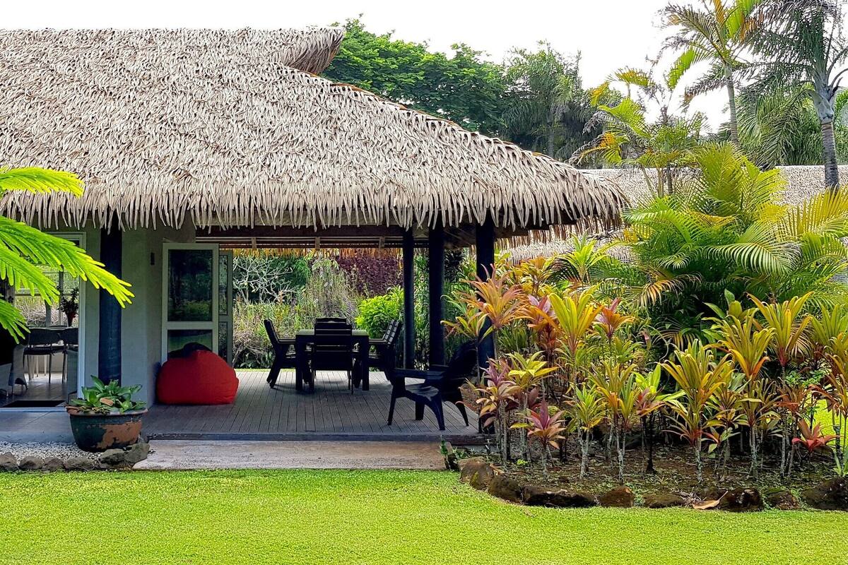 A thatched-roof structure with a dining area and a large potted plant.