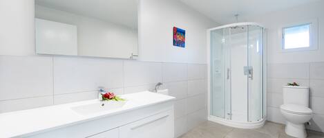 A modern bathroom with a white vanity, a glass shower enclosure, and a toilet.