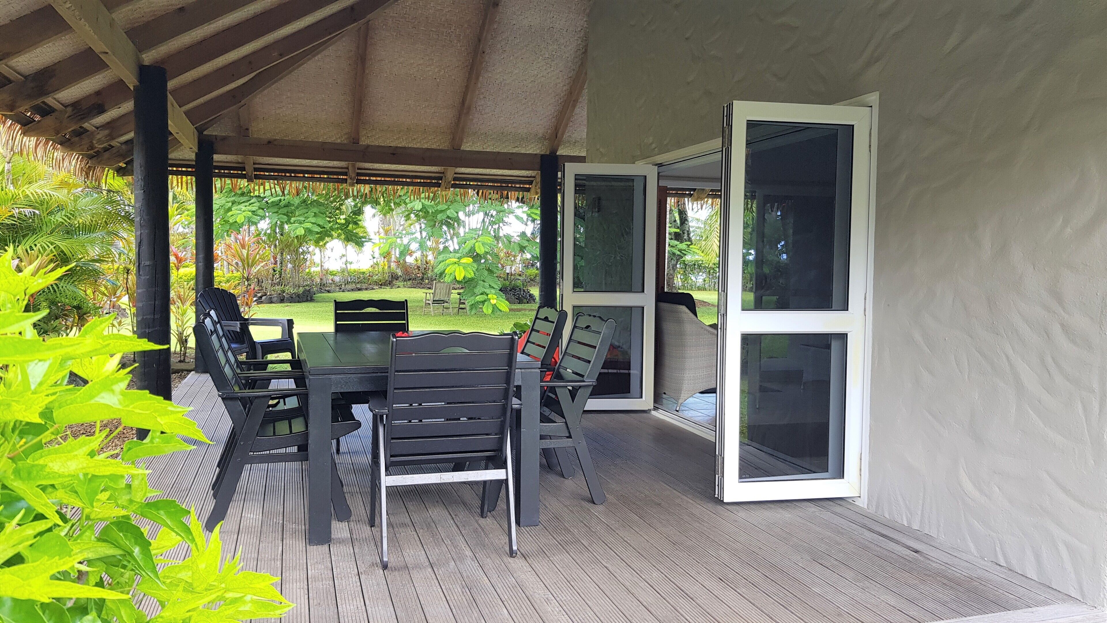 Un patio exterior con mesa y sillas, rodeado de un espacio cubierto con vistas a un jardín.