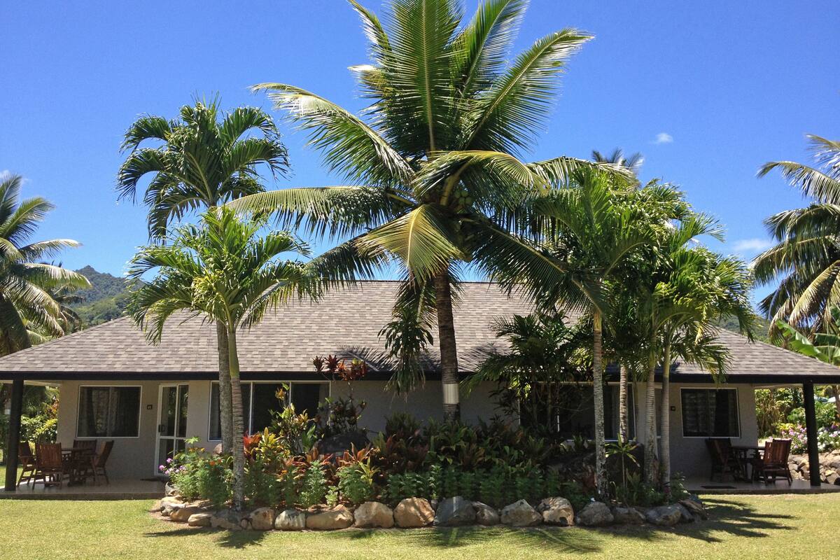 A house with a tiled roof, surrounded by a well-maintained lawn and palm trees.