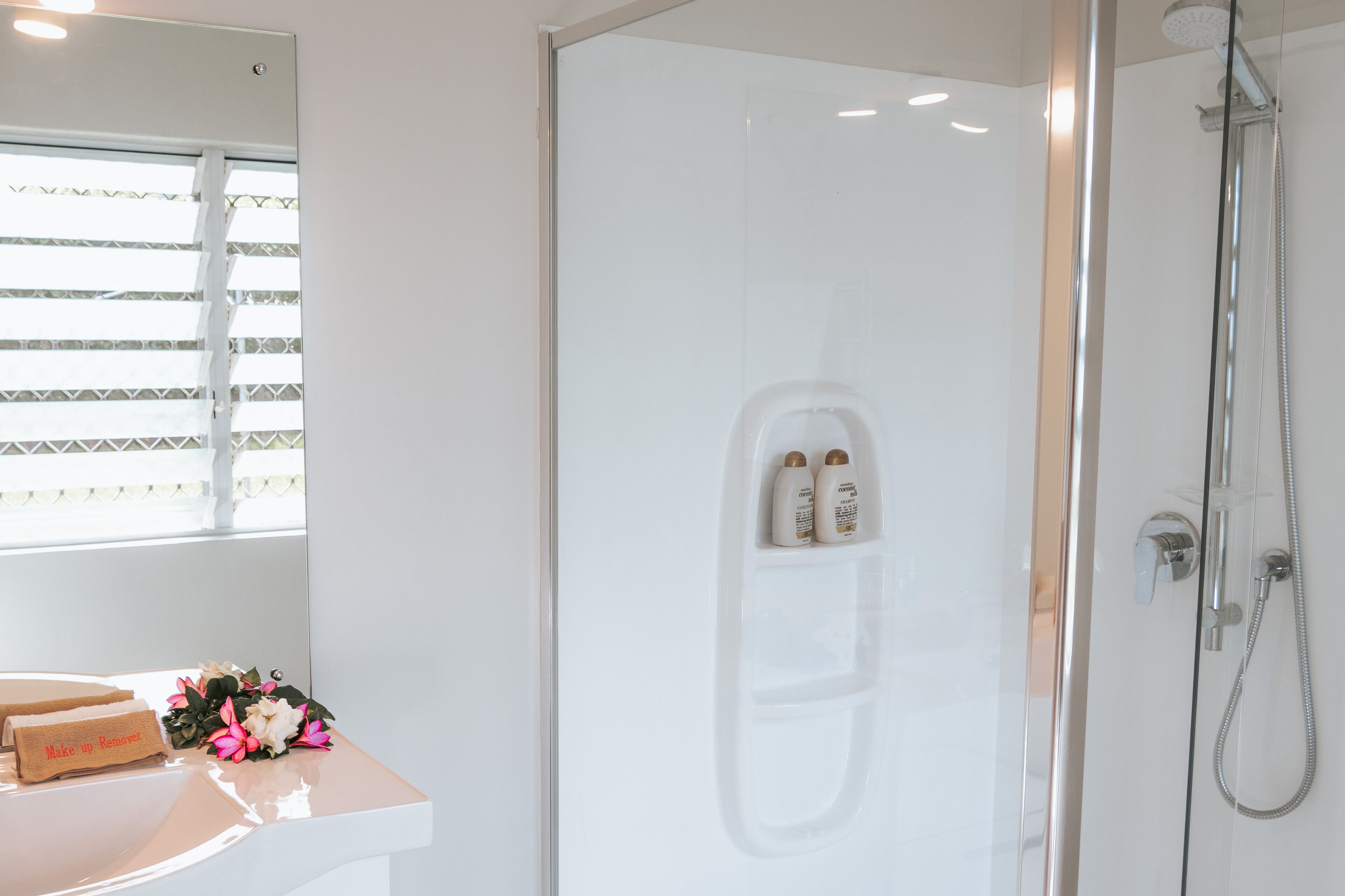 Een moderne badkamer met een douchecabine van glas, een wastafel met spiegel en een raam met jaloezieën.