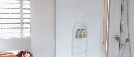 A modern bathroom with a glass shower enclosure, a vanity with a mirror, and a window with blinds.