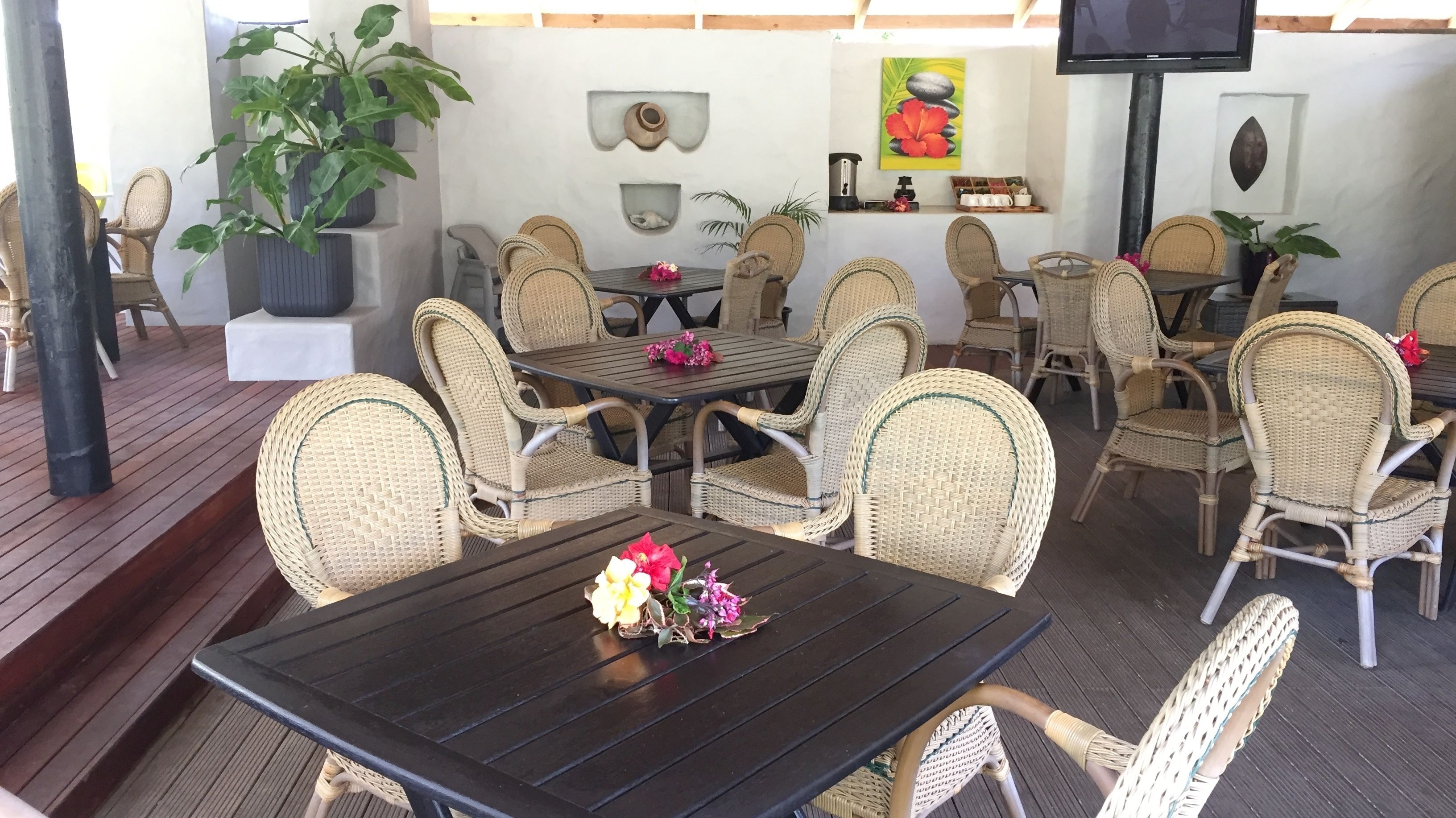 An outdoor dining area with wicker furniture and a black table, surrounded by potted plants and decorative wall art.