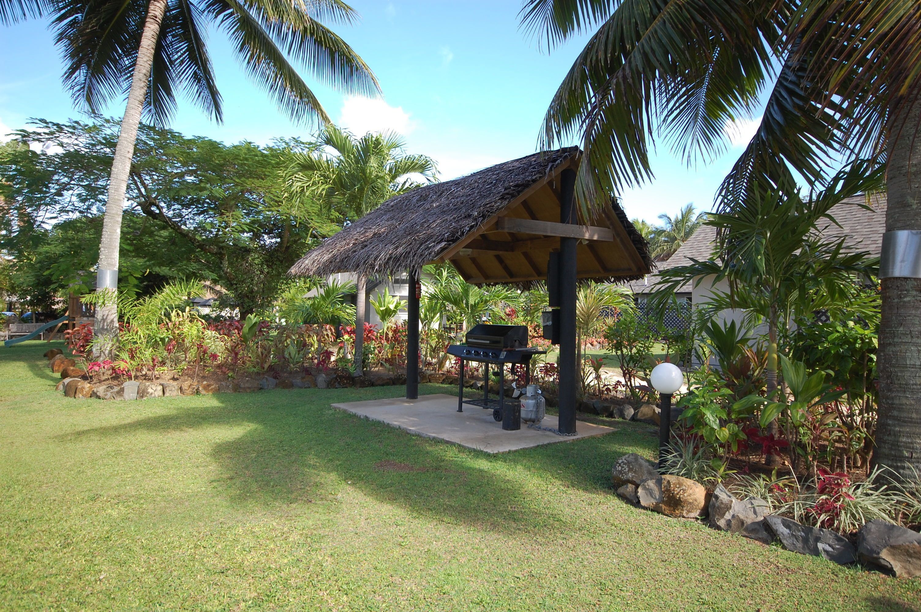 Un espacio al aire libre techado con una parrilla, rodeado de plantas tropicales y palmeras.