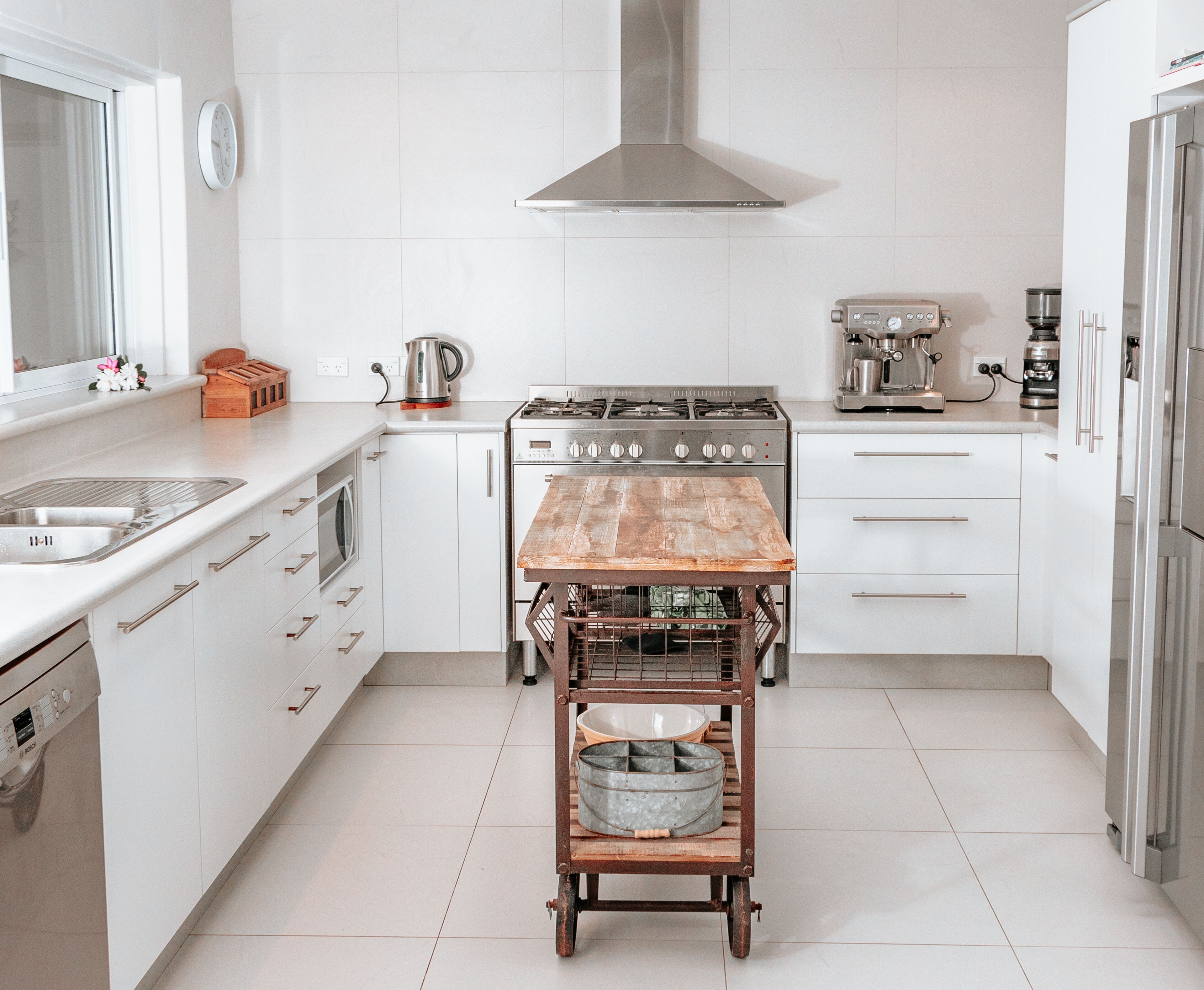 Una cocina moderna con muebles blancos, una estufa de acero inoxidable y una mesa de madera con un bol metálico.