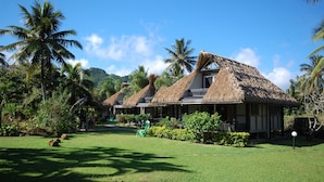 A resort with thatched-roof cottages, lush greenery, and a clear blue sky. - Lagoon Breeze Villas (Rarotonga)