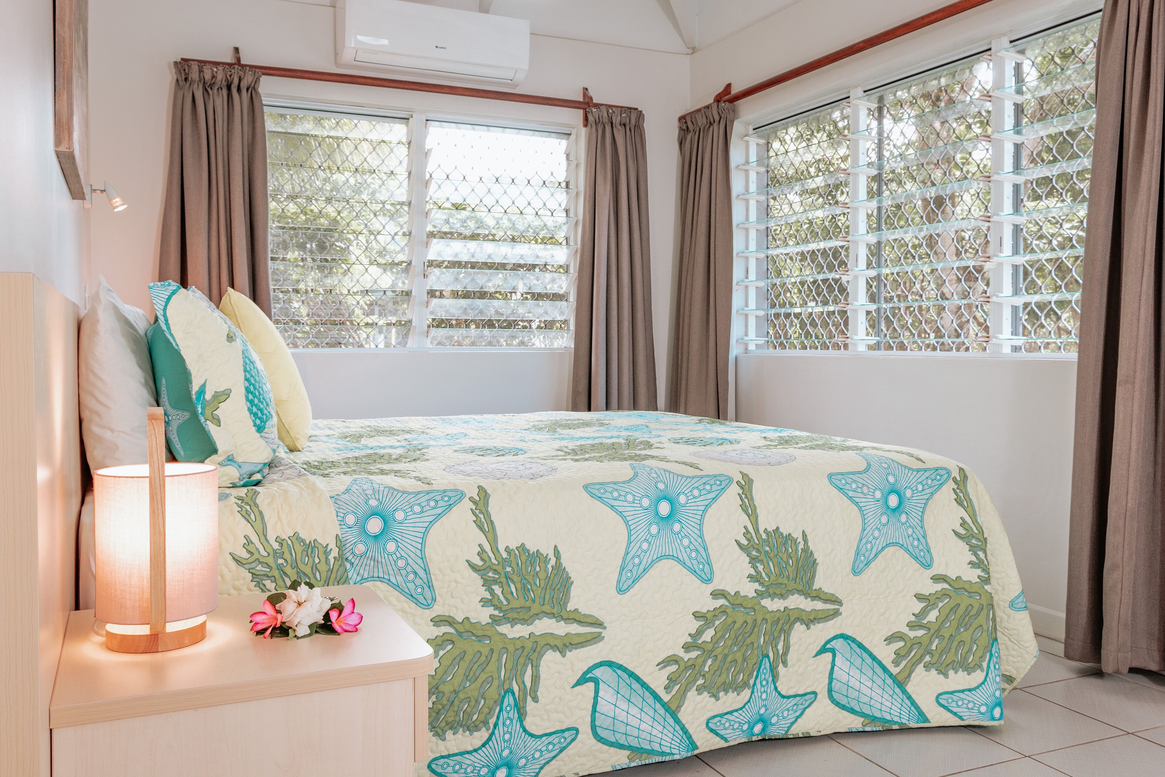 Quarto com cama, cortinas, abajur e janela com vista.