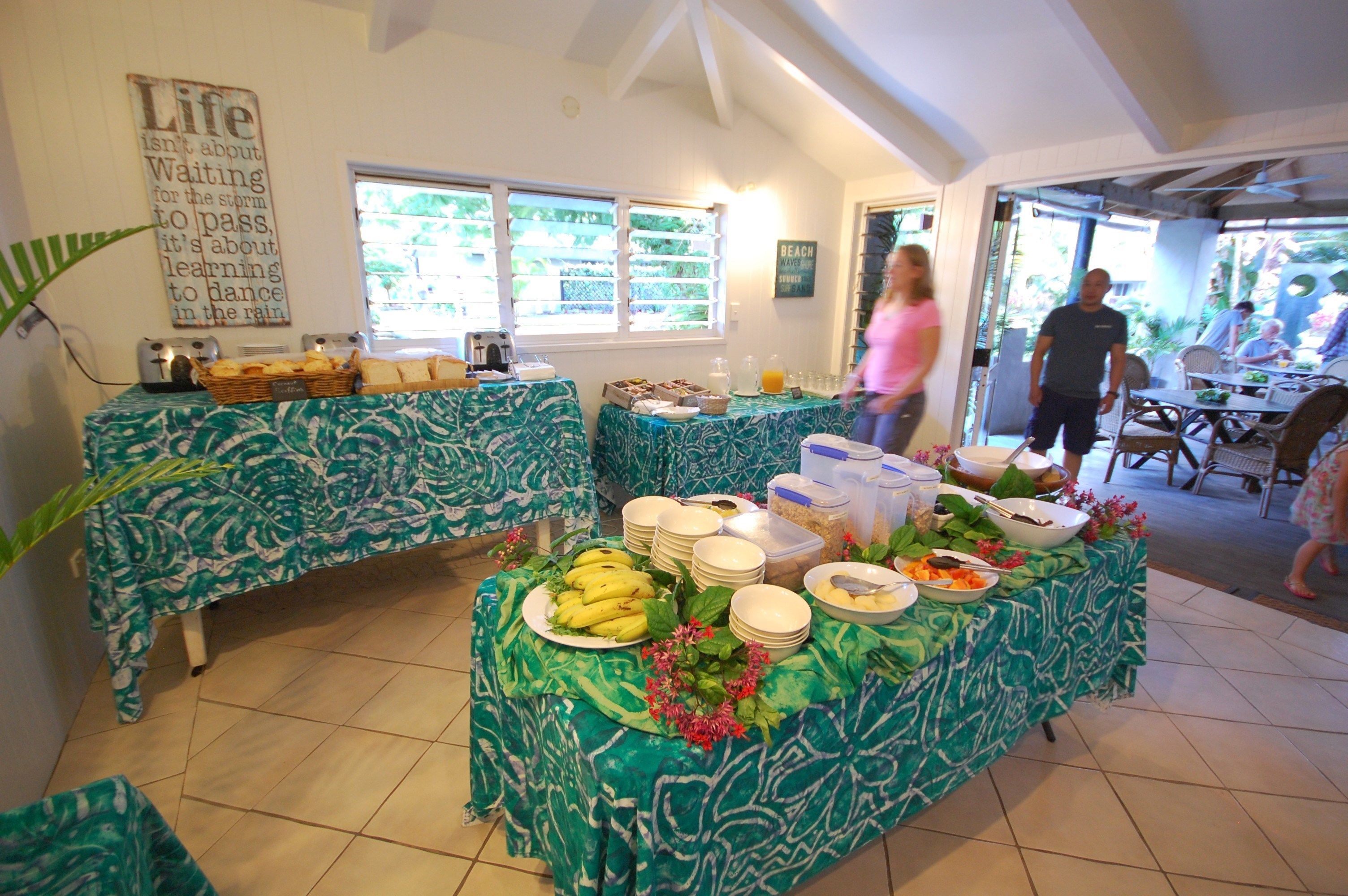 A buffet setup with tropical-themed tablecloths, a variety of food items, and a motivational quote on the wall.