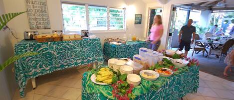 A buffet setup with tropical-themed tablecloths, a variety of food items, and a motivational quote on the wall.