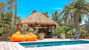 A pool area with a thatched-roof gazebo, wooden deck, and tropical plants. - Lagoon Breeze Villas (Rarotonga)